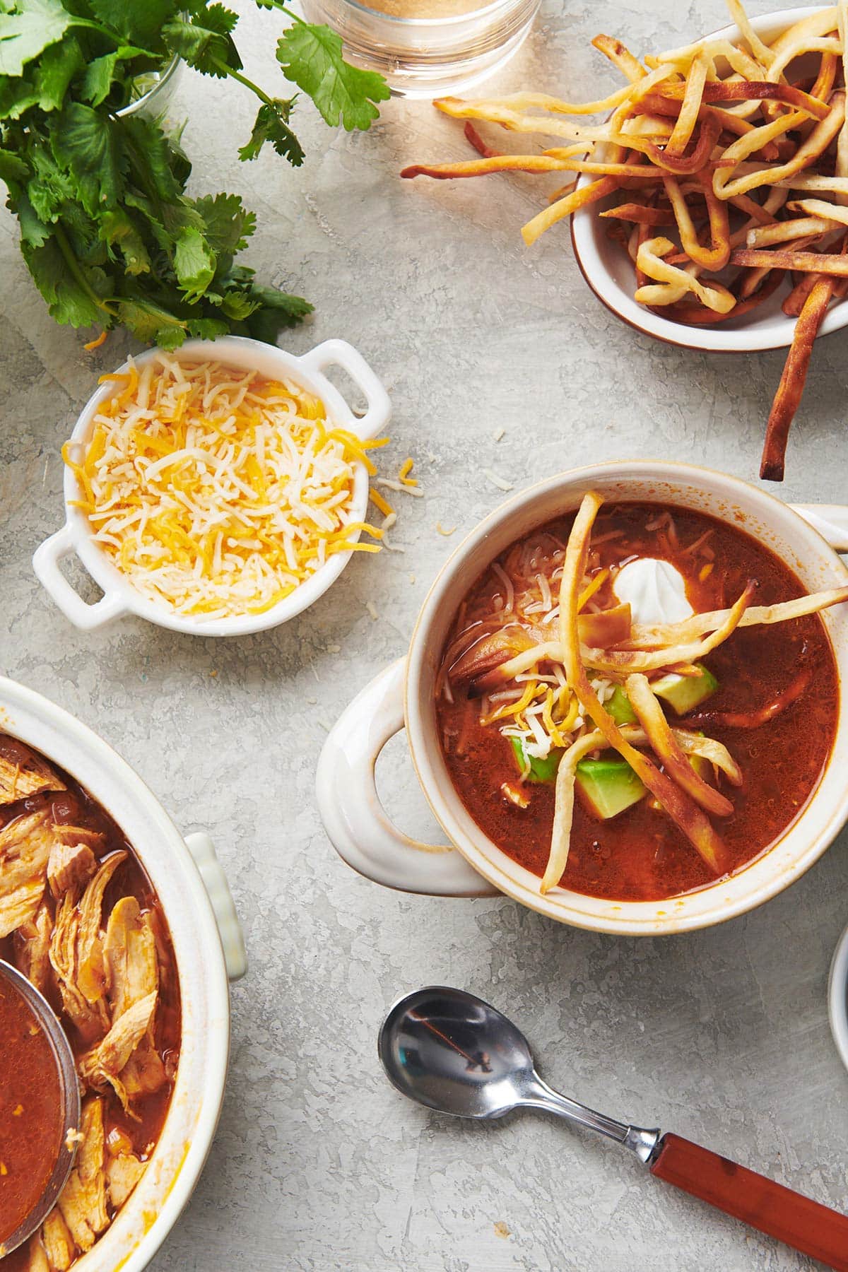 Bowl of Mexican Chicken Tortilla Soup on table with cheese, tortilla strips, and other toppings.