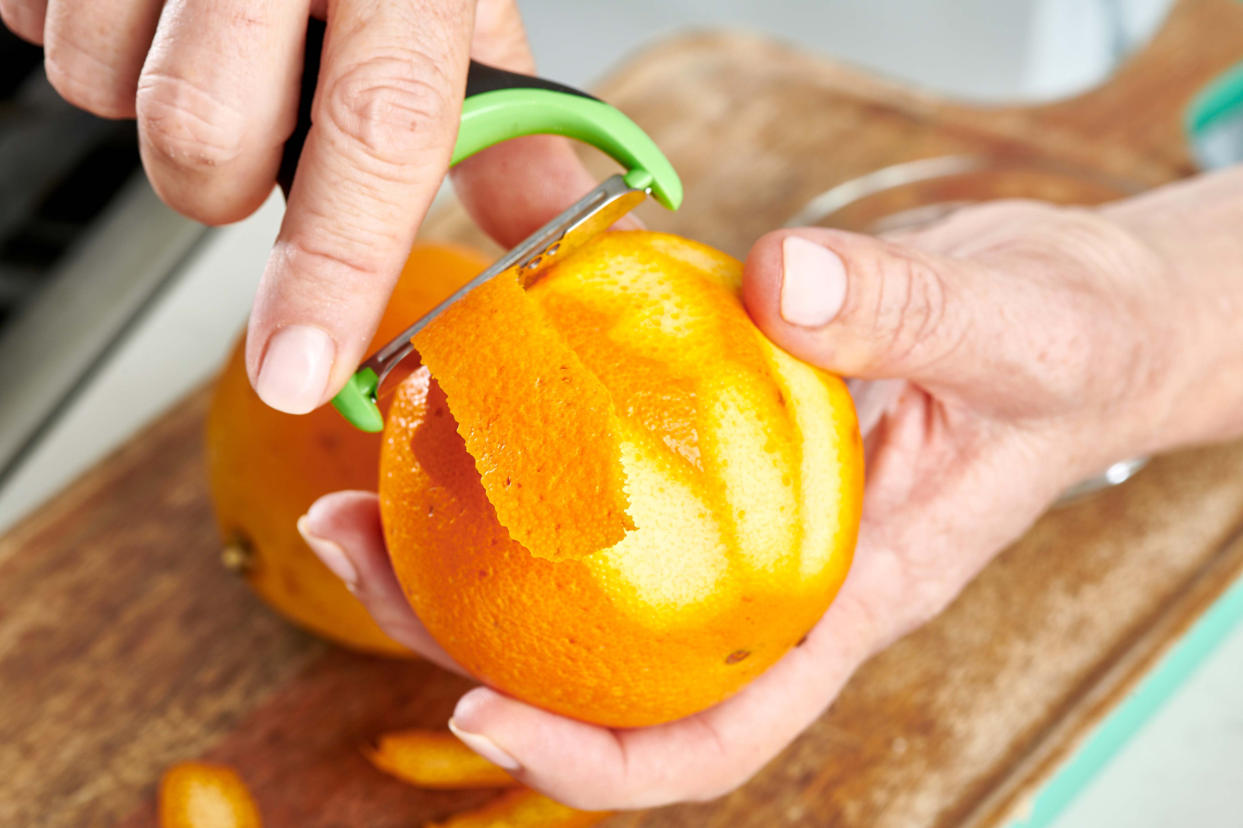 Woman using a peeler on an orange.