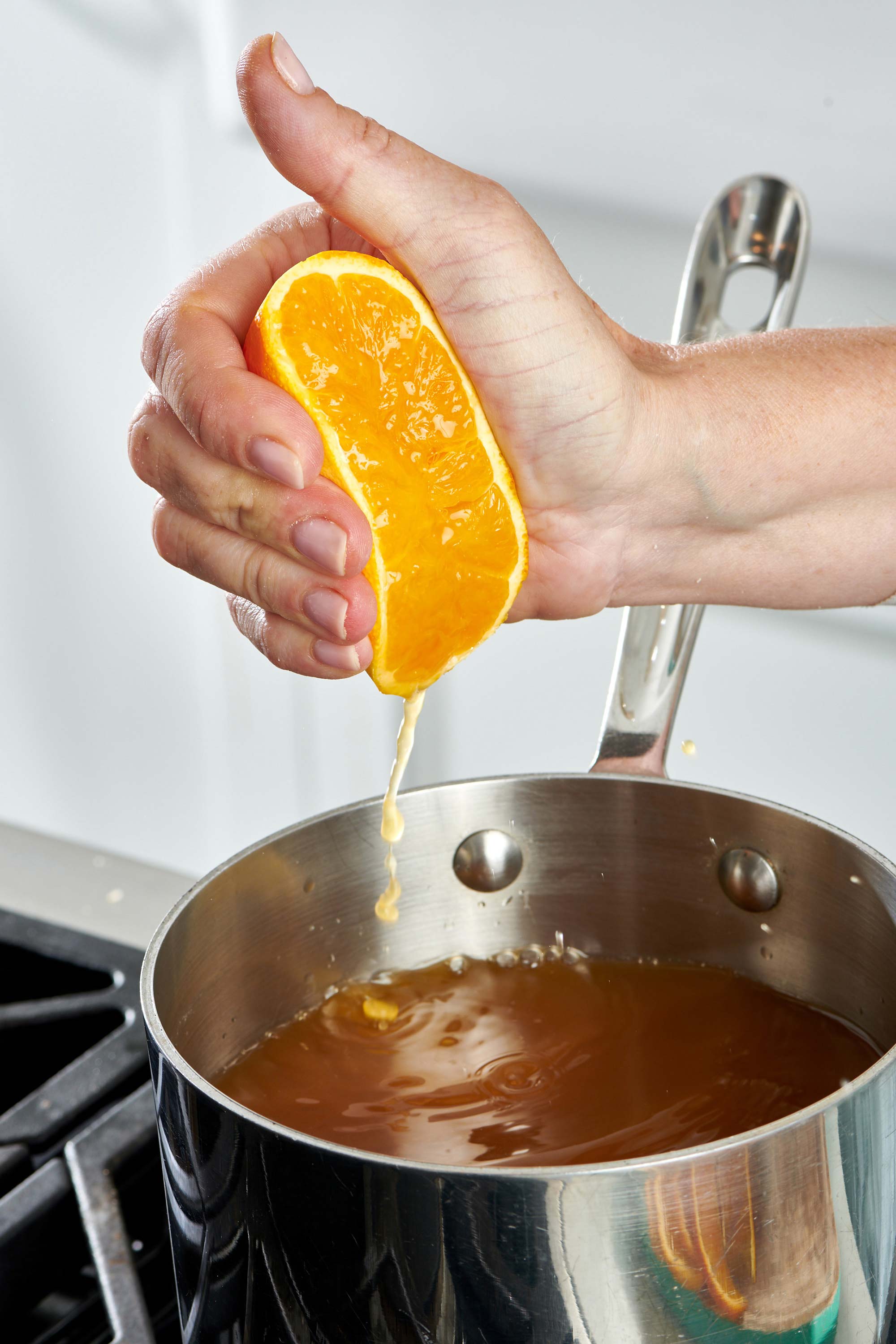 Woman squeezing half an orange into a pot.