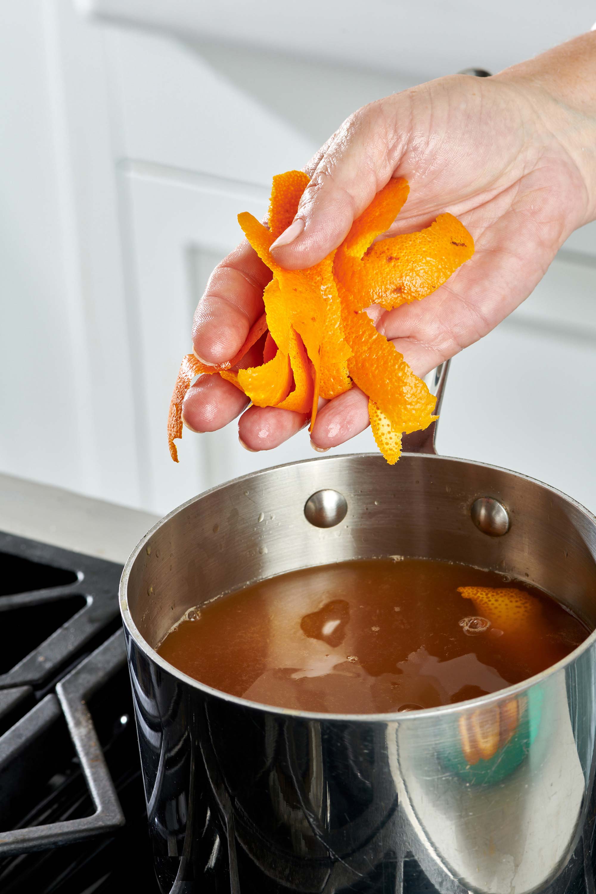 Woman tossing orange peels into a pot.