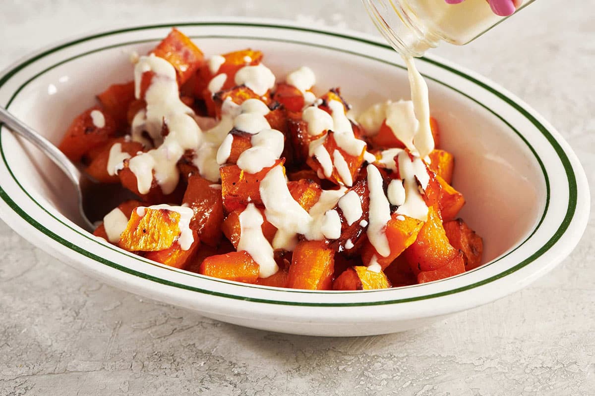 Woman pouring a creamy sauce over Roasted Butternut Squash.