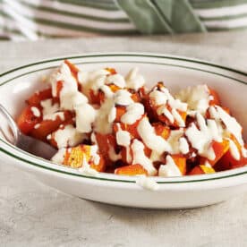 Woman serving roasted butternut squash with cream sauce in white bowl.