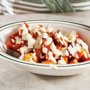 Woman serving roasted butternut squash with cream sauce in white bowl.