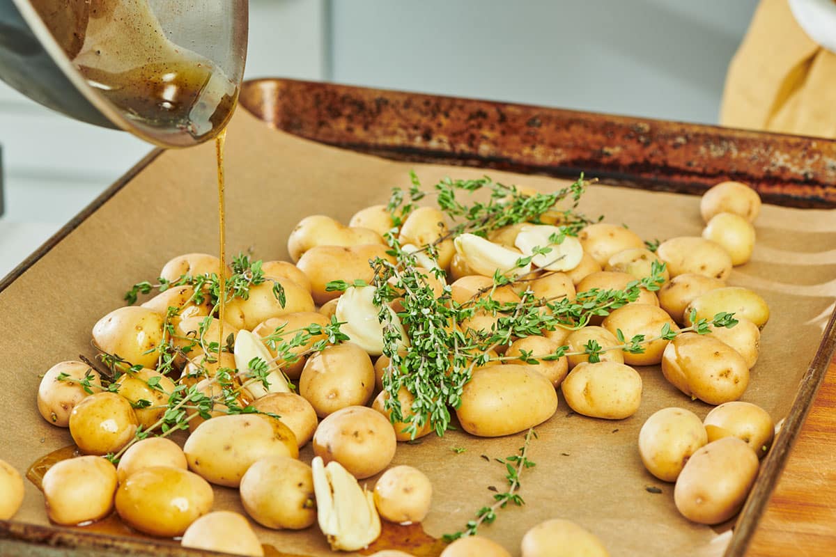 Drizzling duck fat over fresh thyme and potatoes on baking sheet.