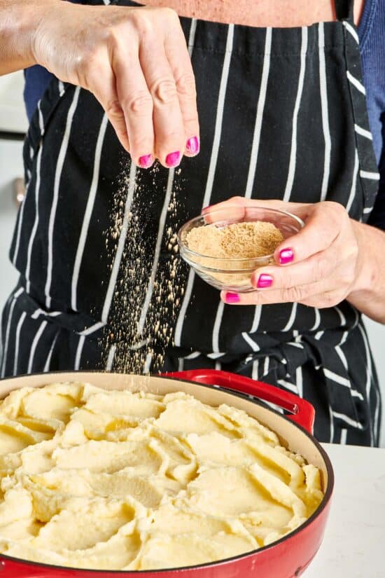 Woman drizzling bread crumb topping onto a Dutch oven of mashed potatoes.