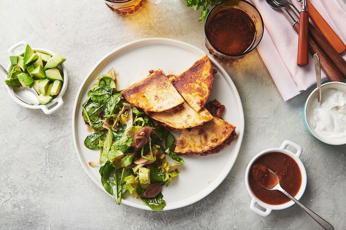 Sliced quesadilla with beef chili and cheese on plate with salad.