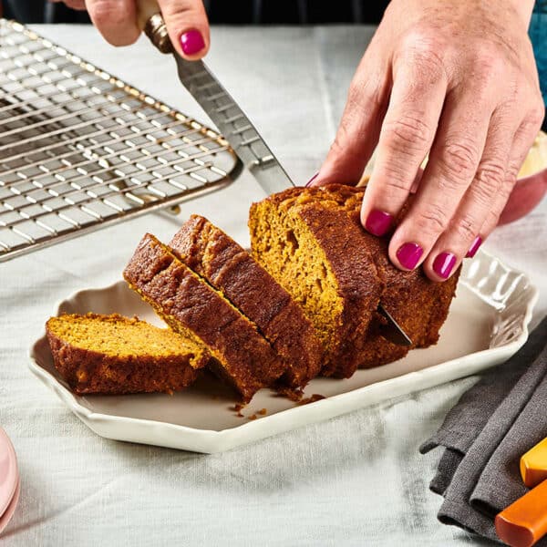 Woman slicing pumpkin bread with knife on white plate.