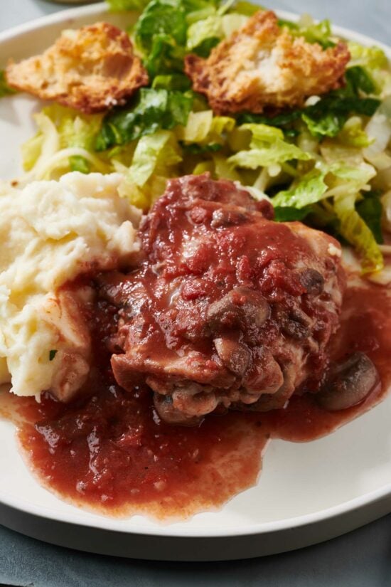 Chicken Cacciatore on a plate with mashed potatoes and salad.