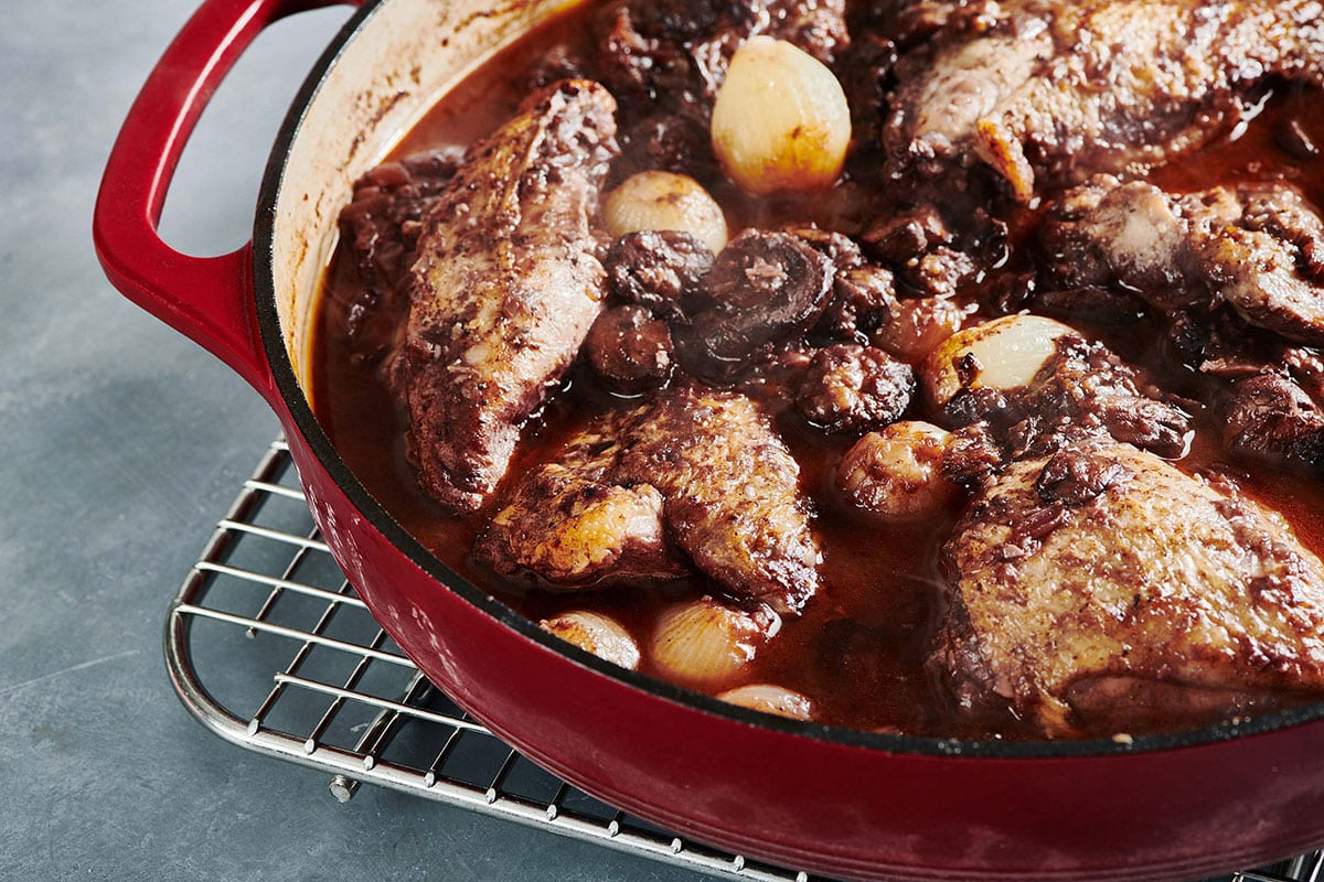 Coq au Vin in a red Dutch oven on a wire rack.