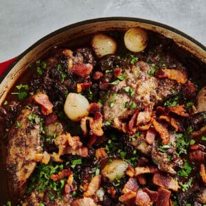Coq au vin in large red cast-iron skillet on table.