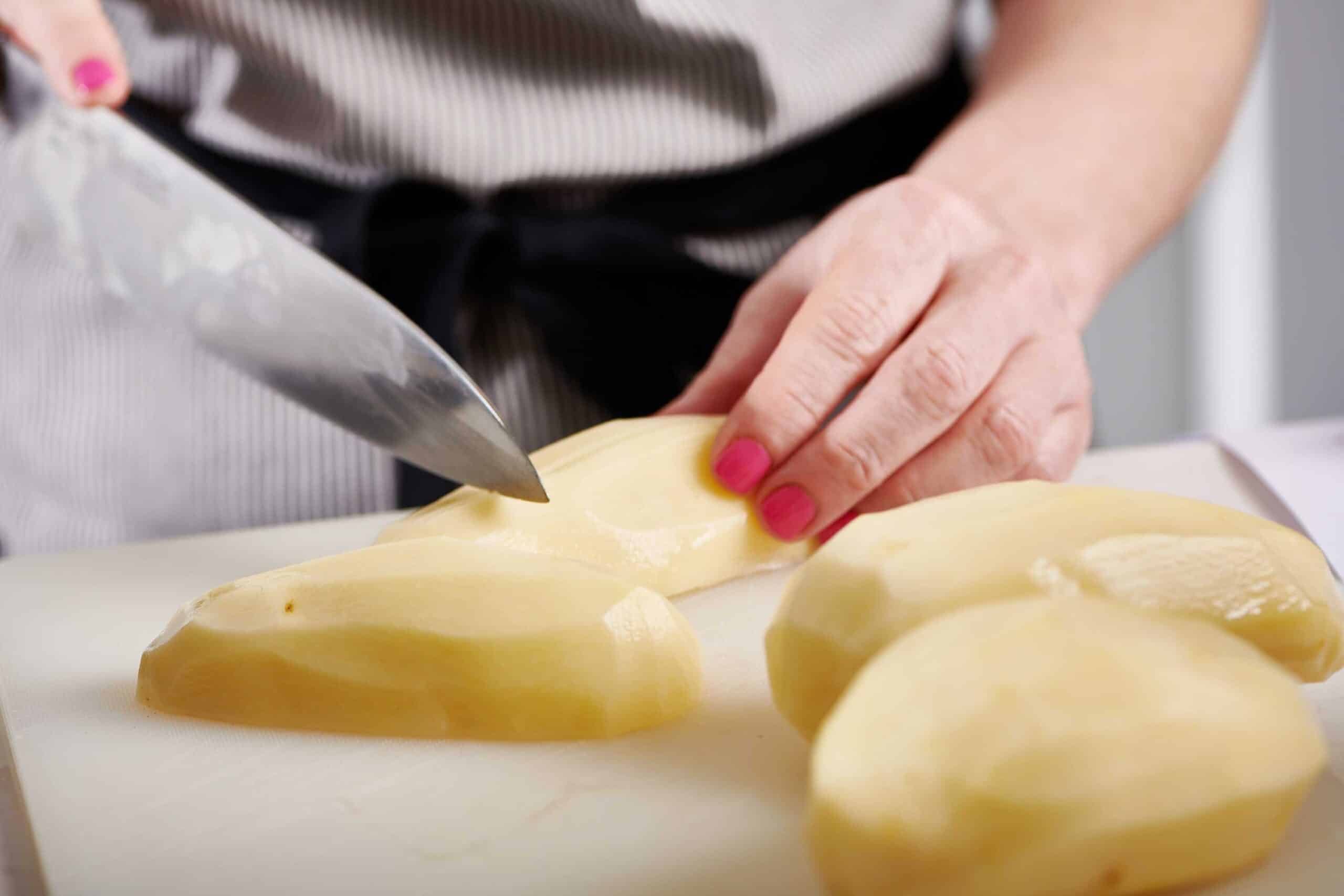 Slicing potatoes on cutting board with chef knife.