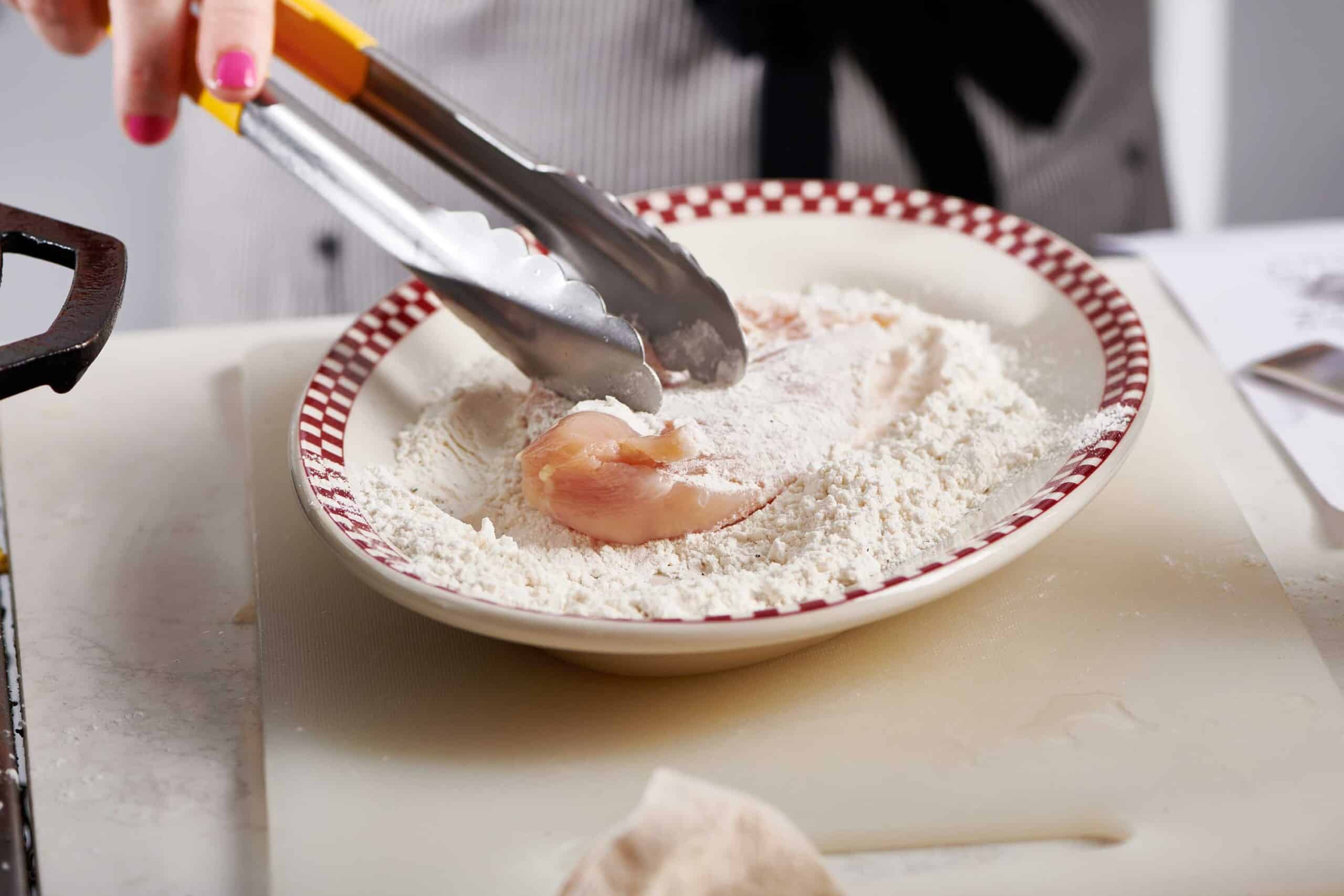 Dredging chicken breasts in flour.