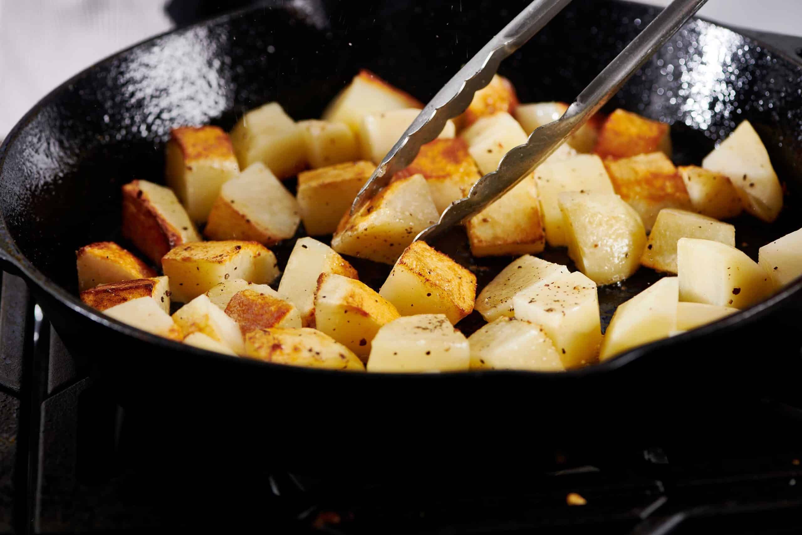 Tongs grabbing a diced potato from a pan.