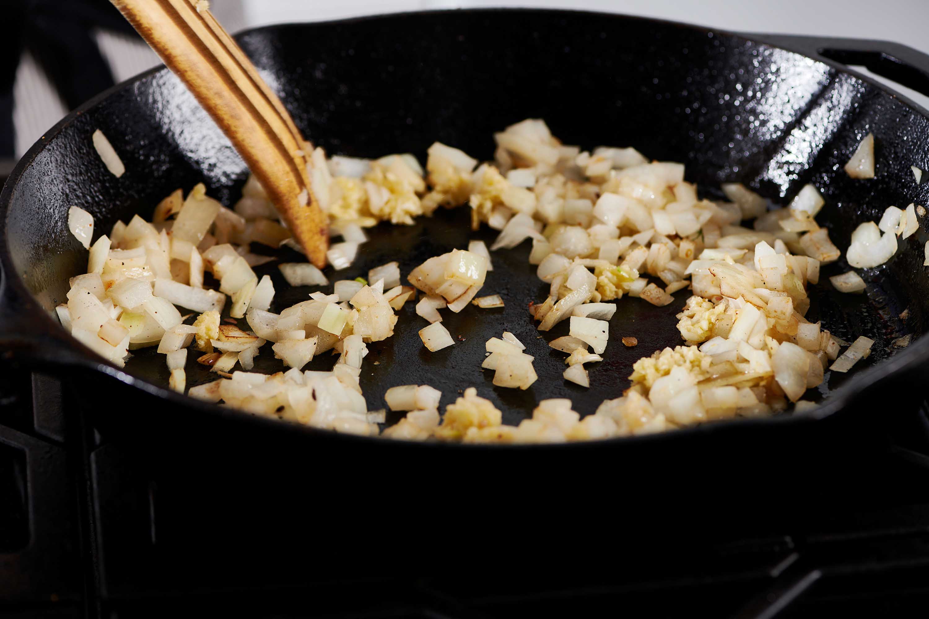 Wooden spatula stirring a skillet of diced onions.