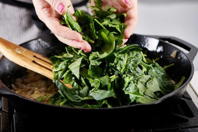 Woman adding spinach to a skillet.