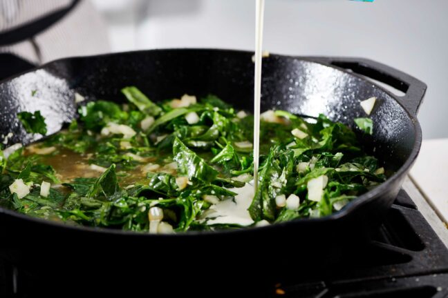 Cream pouring into a skillet with spinach and onions.