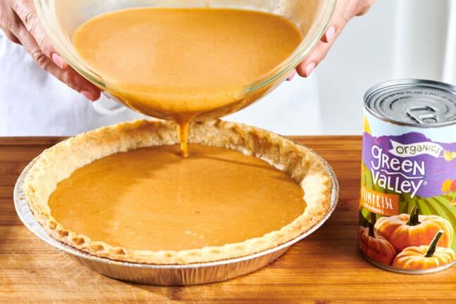 Woman pouring pumpkin filling into a pie crust.