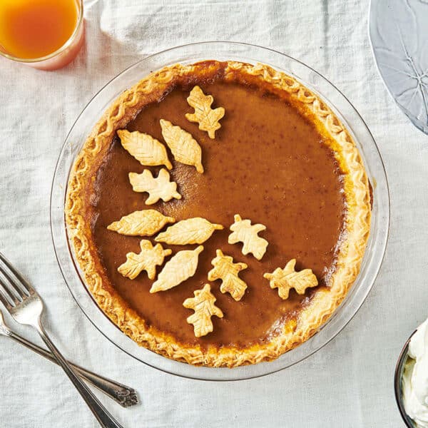 Homemade pumpkin pie with pastry leaf decorations on table.