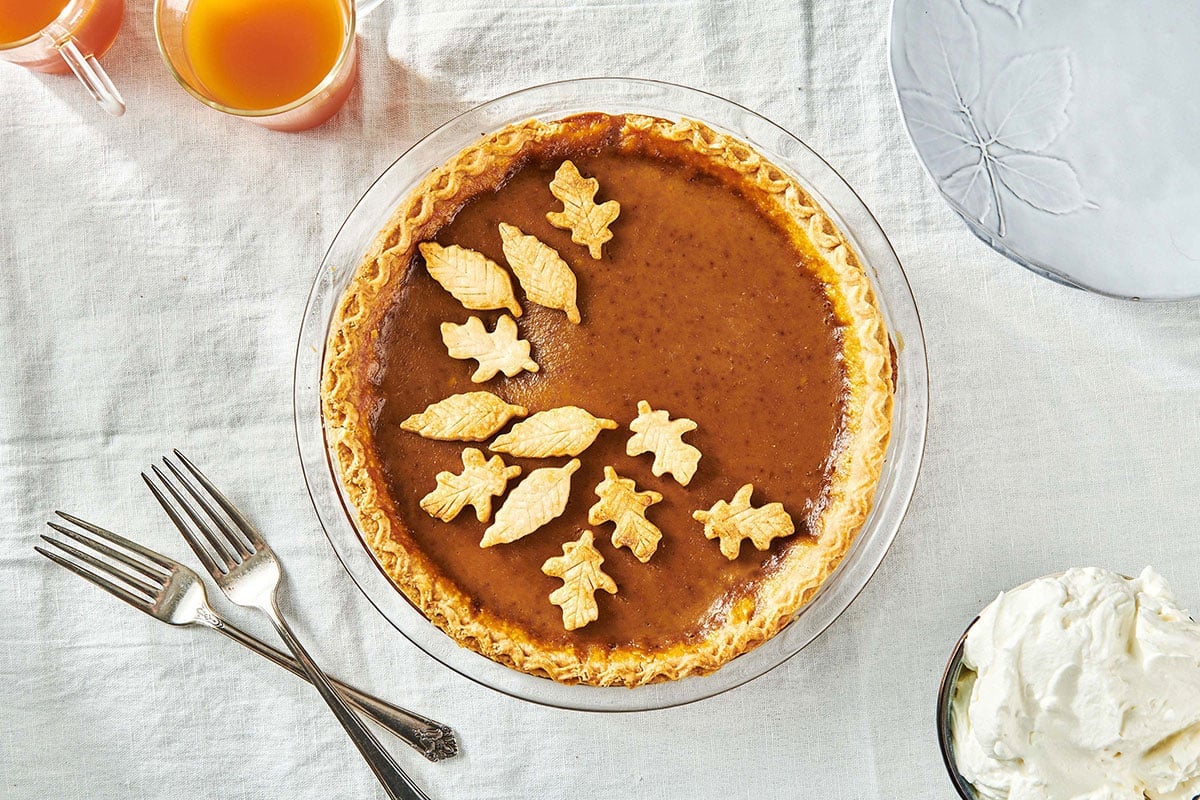Homemade pumpkin pie with pastry leaf decorations on table.
