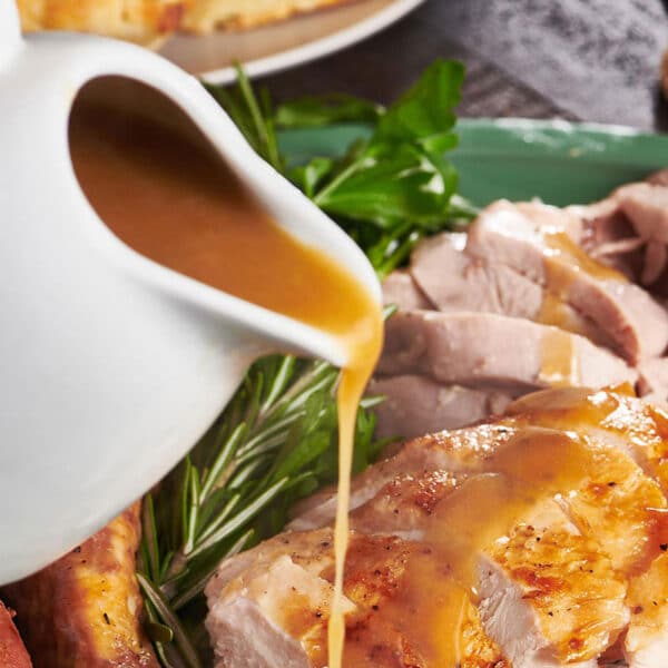 Pouring homemade turkey gravy over slices of roasted turkey on plate.