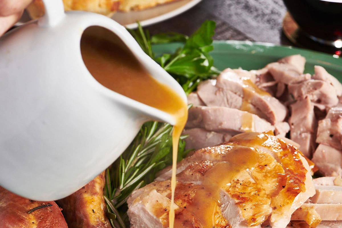 Pouring homemade turkey gravy over slices of roasted turkey on plate.