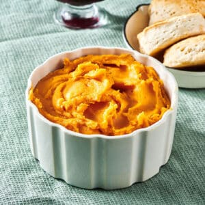 Mashed sweet potatoes in small bowl on table near biscuits.