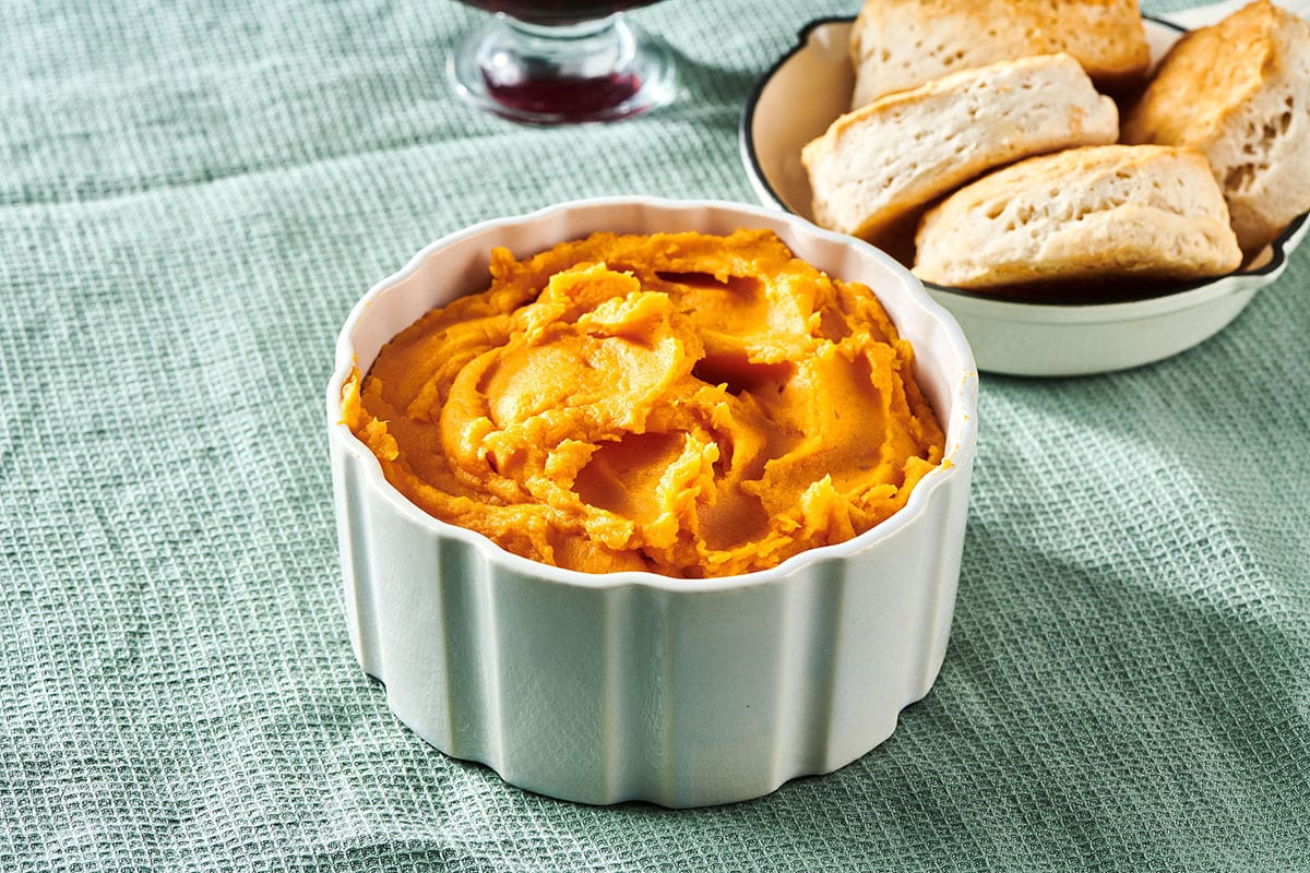 Mashed sweet potatoes in small bowl on table near biscuits.