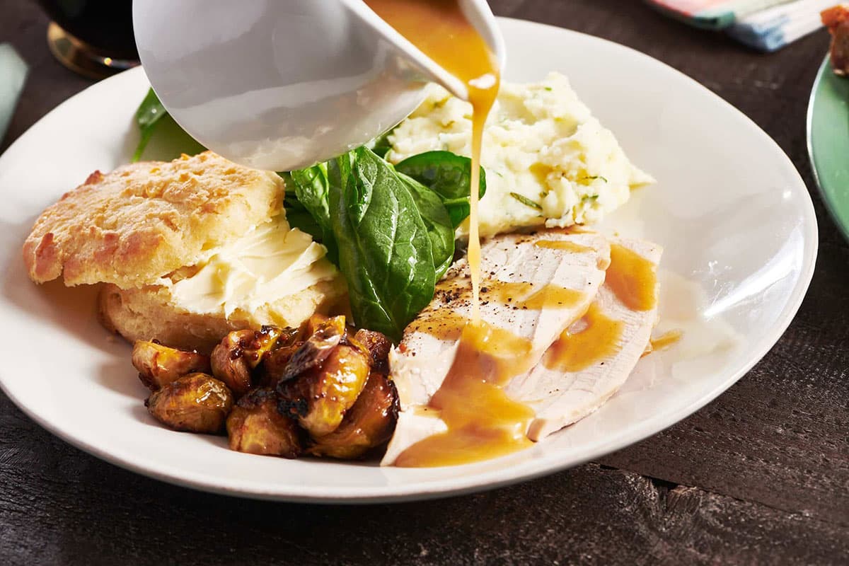 Gravy boat pouring gravy over slices of turkey.