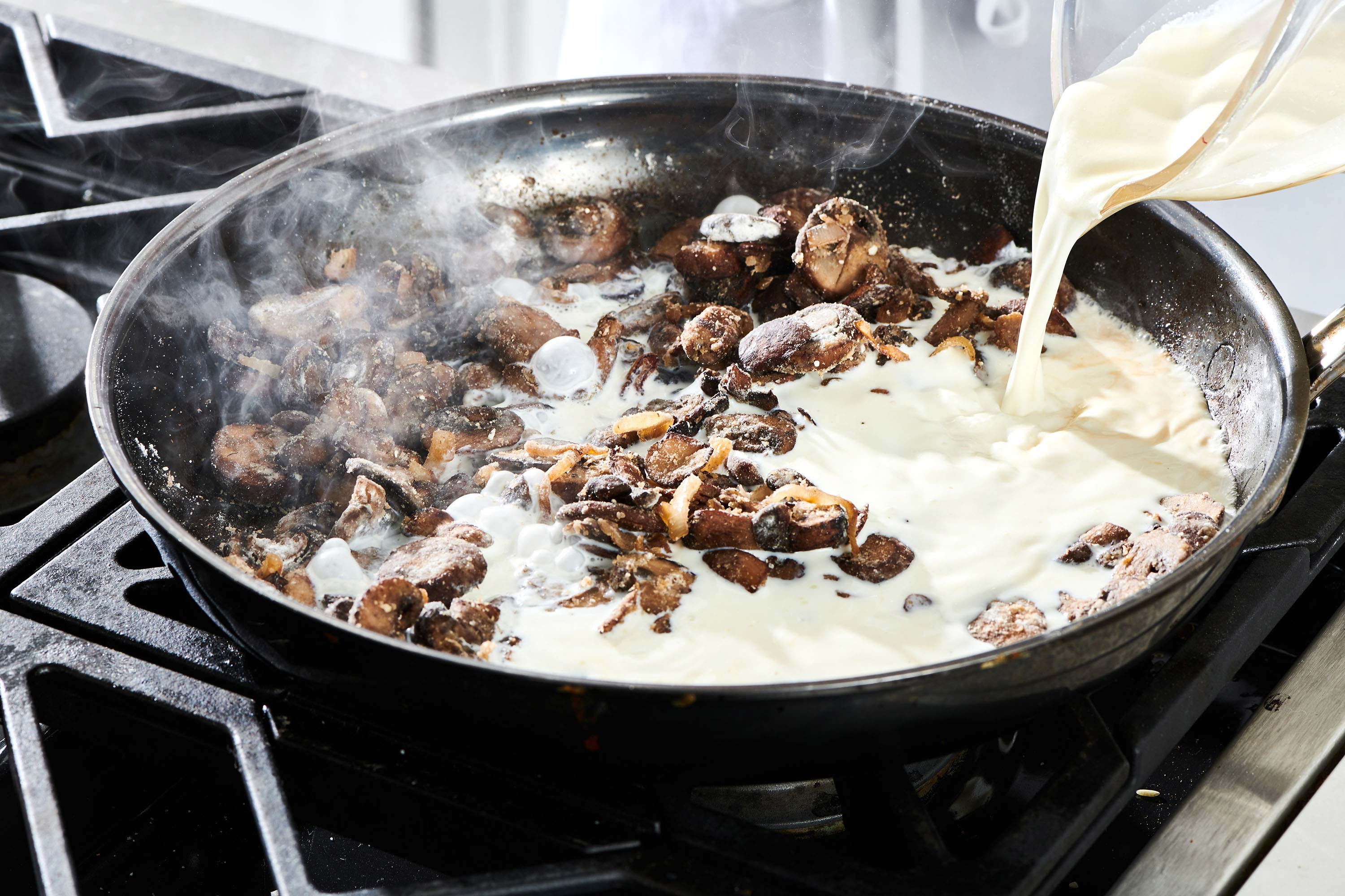 Milk pouring into a skillet of mushrooms.