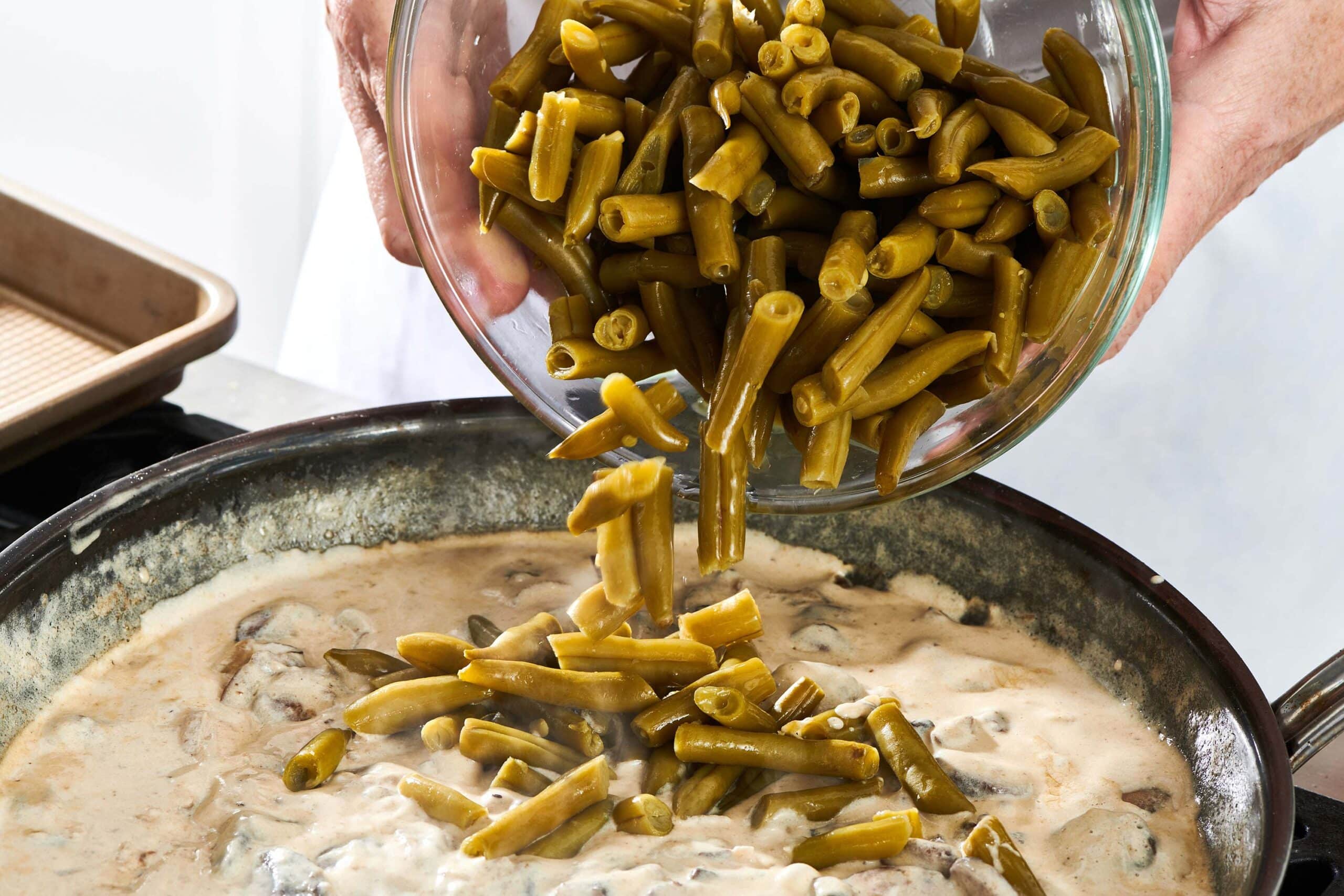Bowl of green beans pouring into a creamy mushroom mixture.