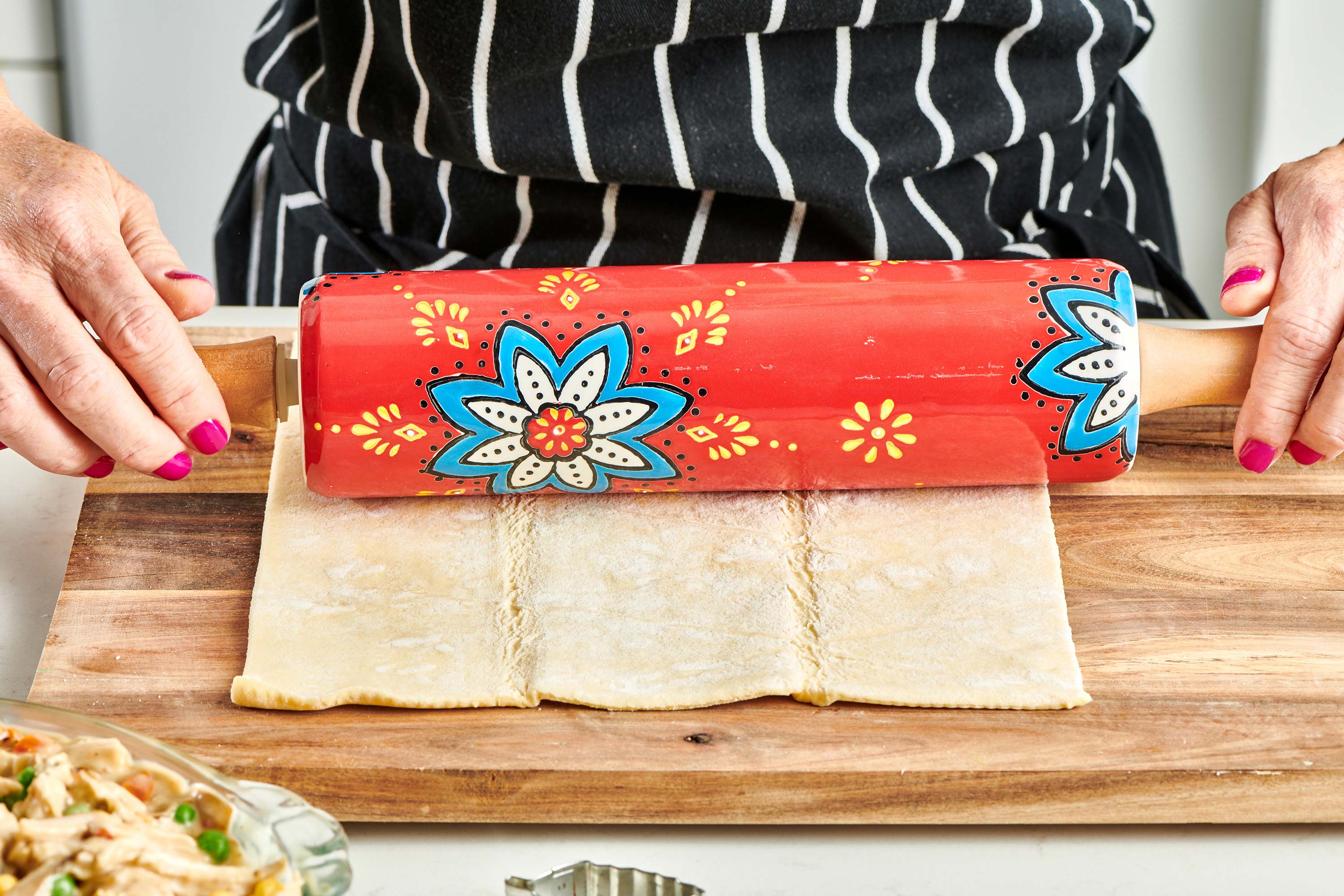 Woman rolling puff pastry sheet on cutting board.