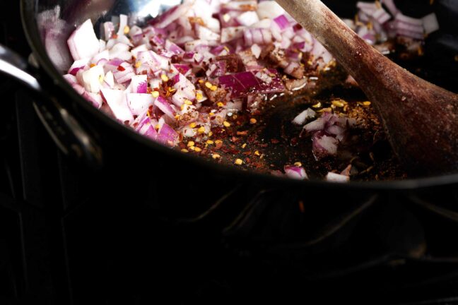 Wooden spoon stirring diced red onions and spices.