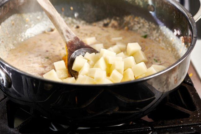 Wooden spoon stirring diced potatoes into a curry mixture.