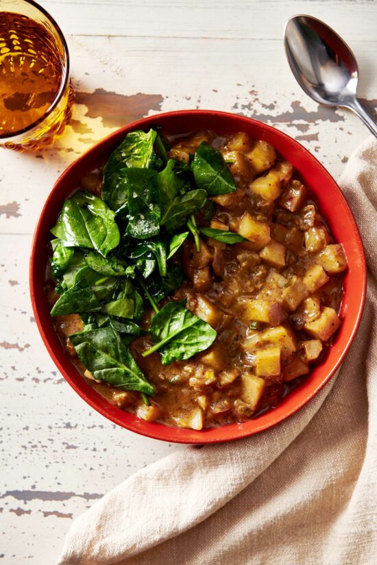 Potato Curry topped with spinach in a red bowl.