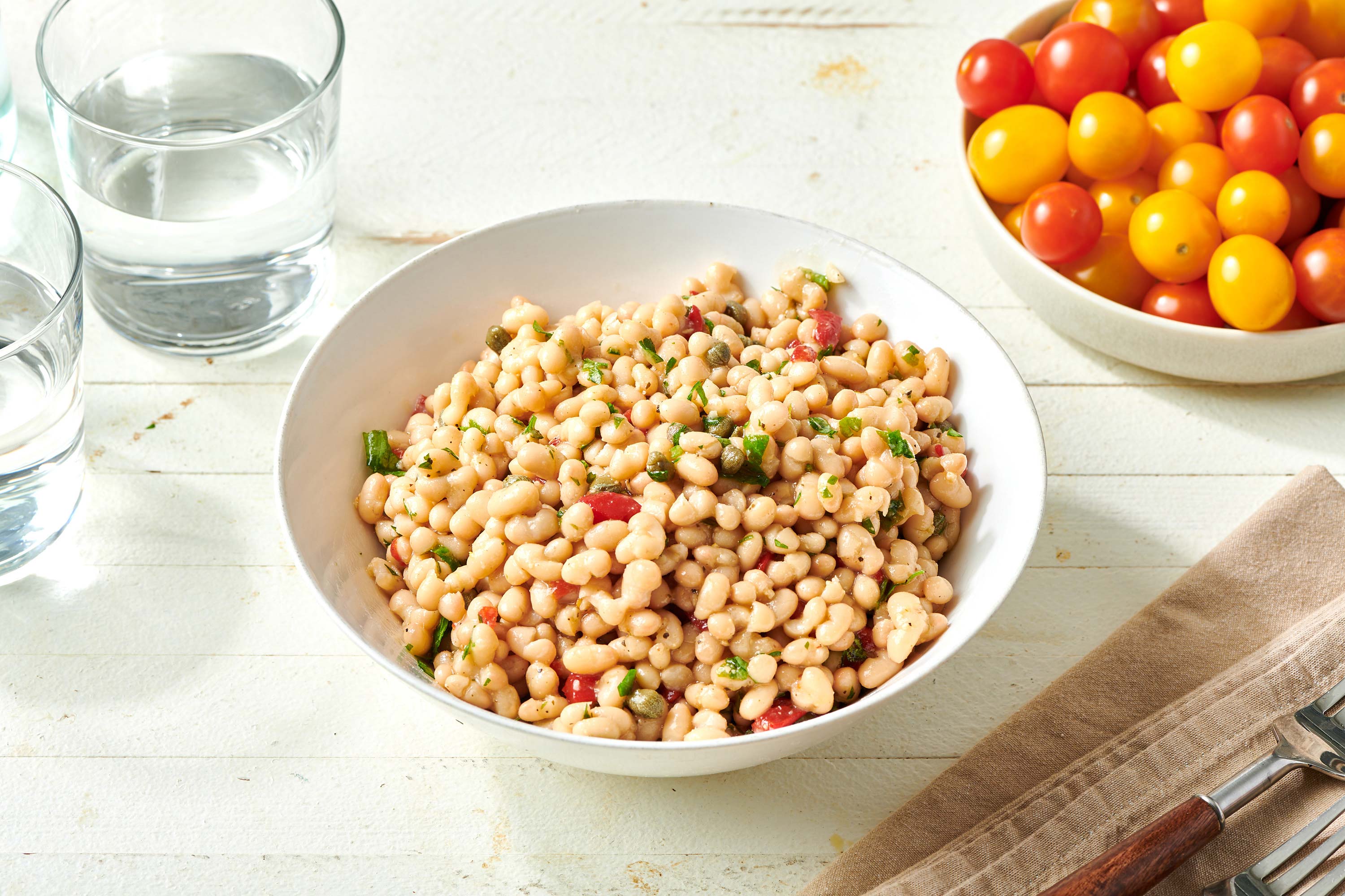 Bowls of tomatoes and White Bean Salad on a white, wooden table.