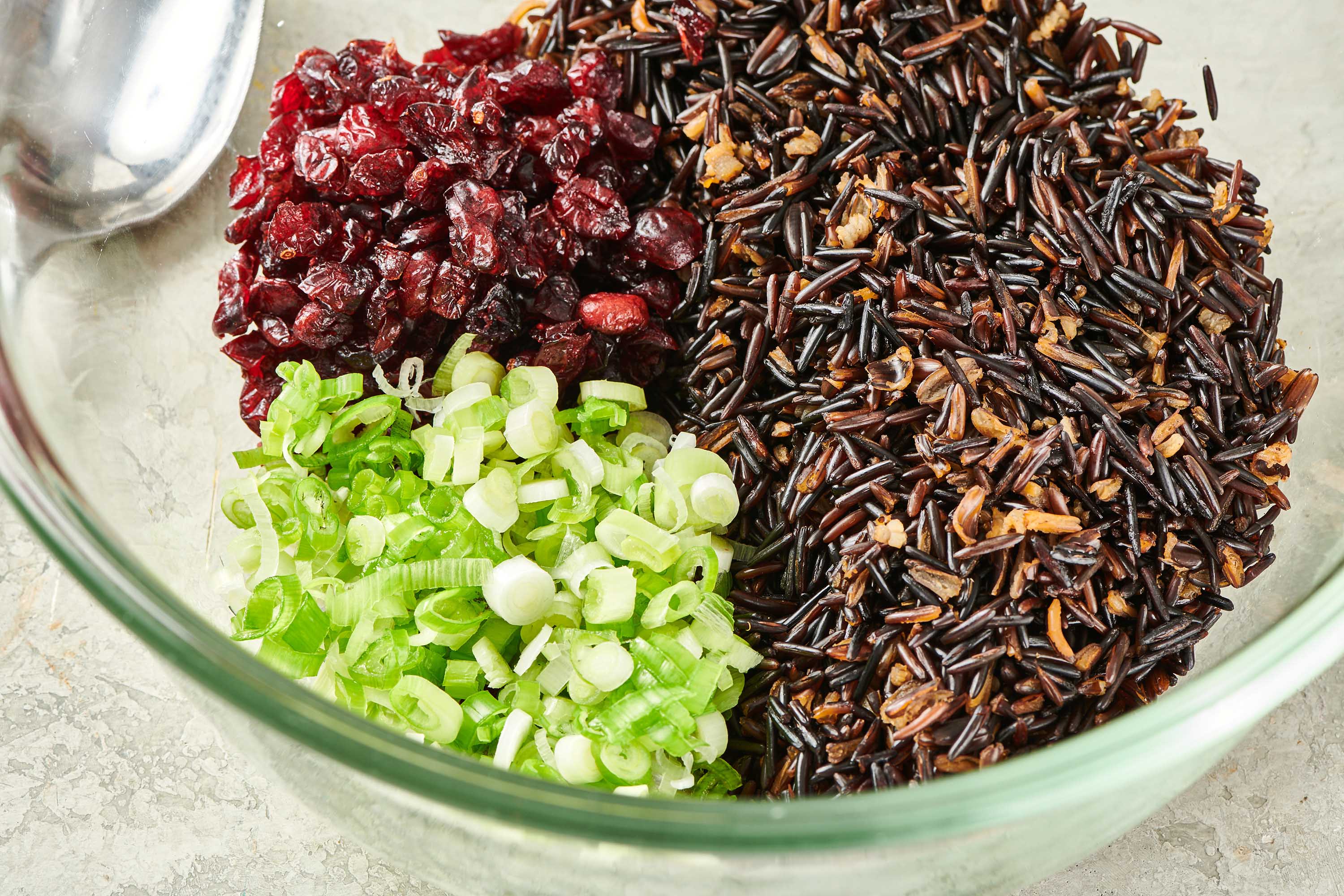 Wild rice, scallions, and dried cranberries unmixed in a bowl.