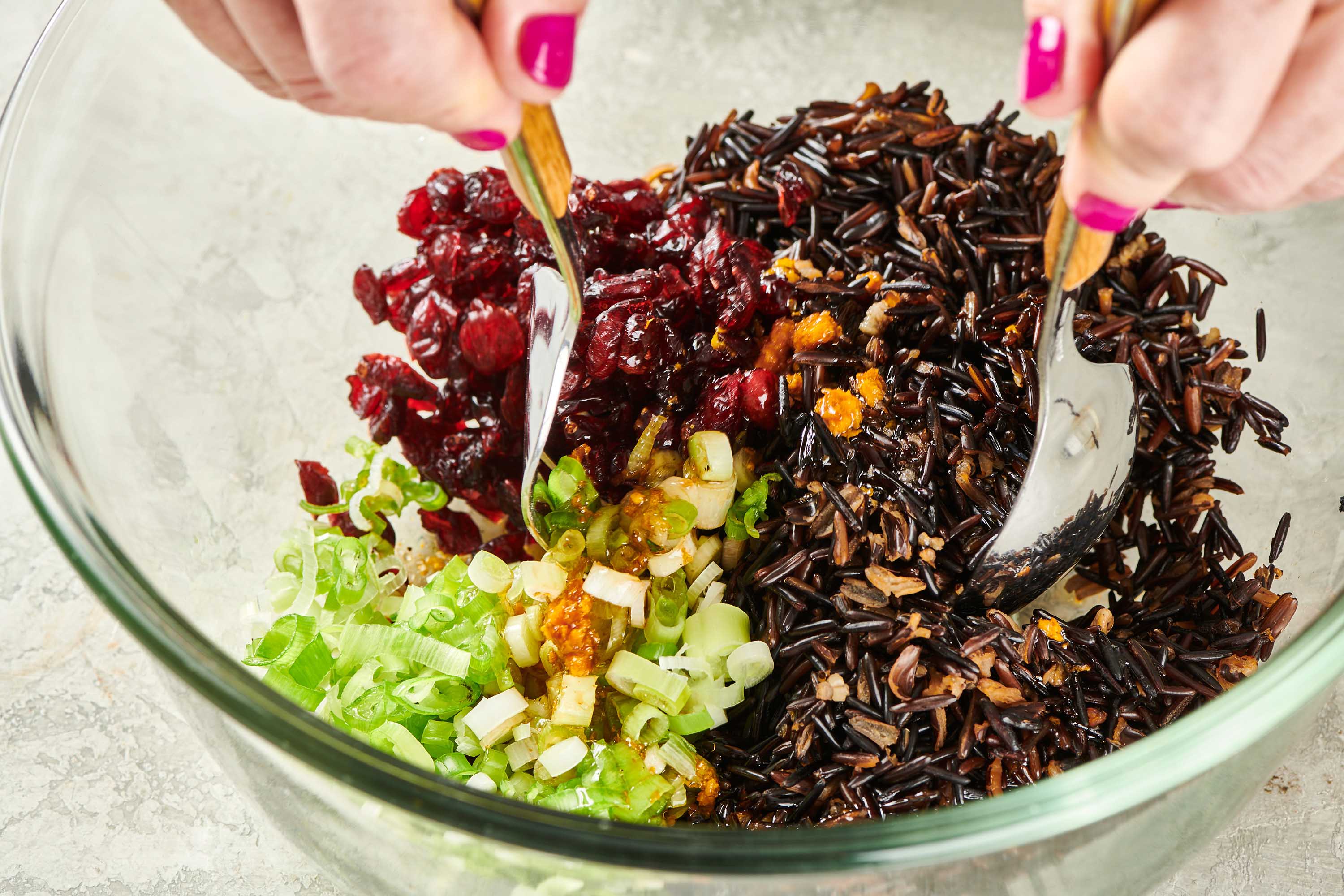 Woman using spoons to mix scallions, dired cranberries, and wild rice.