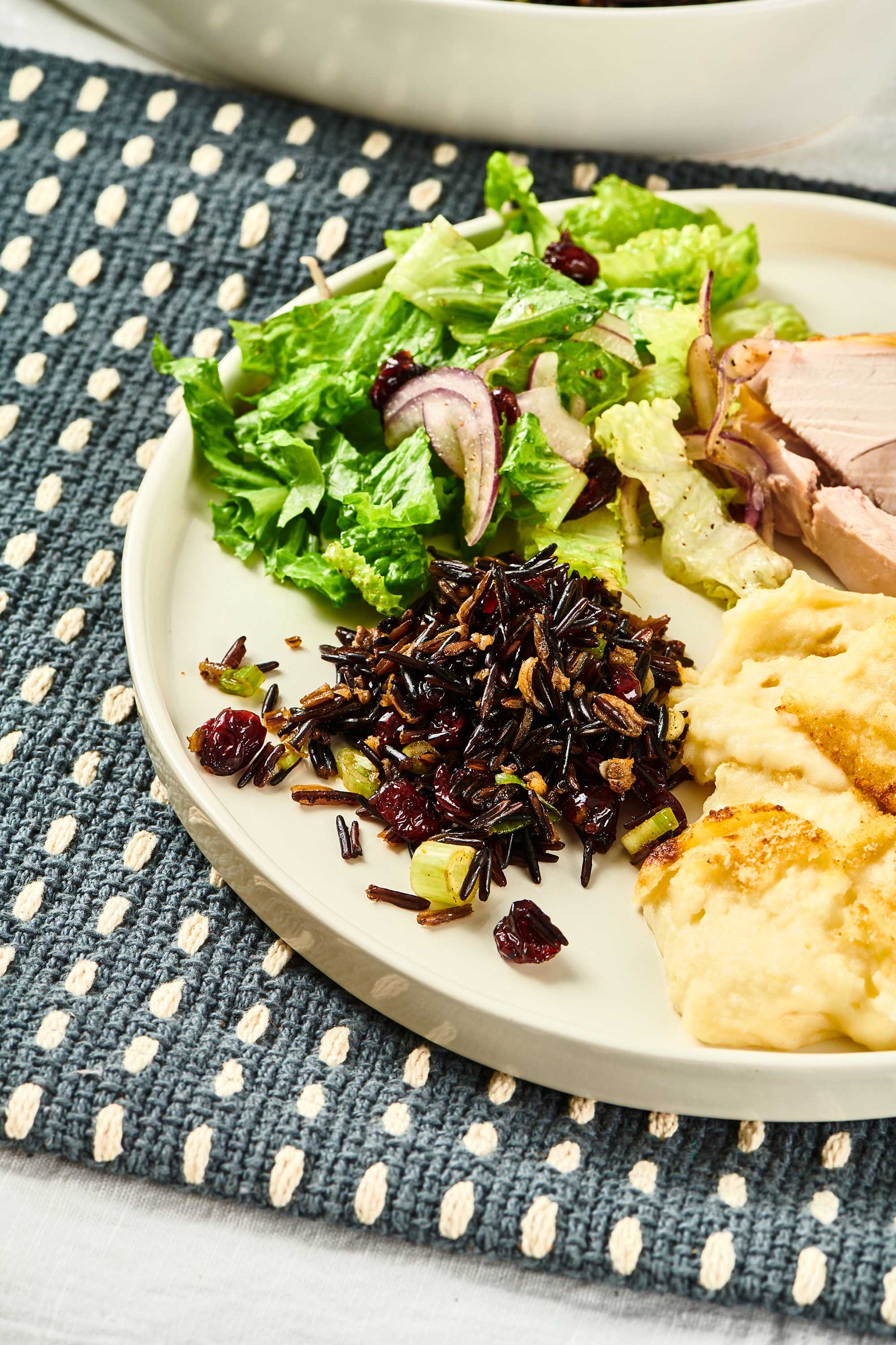 Wild Rice Salad with Cranberries on a plate with mashed potatoes, salad, and meat.