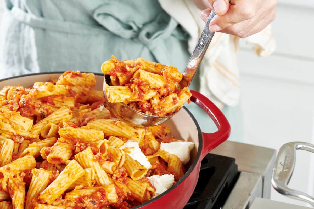 Ladle scooping Baked Ziti from a red pan.
