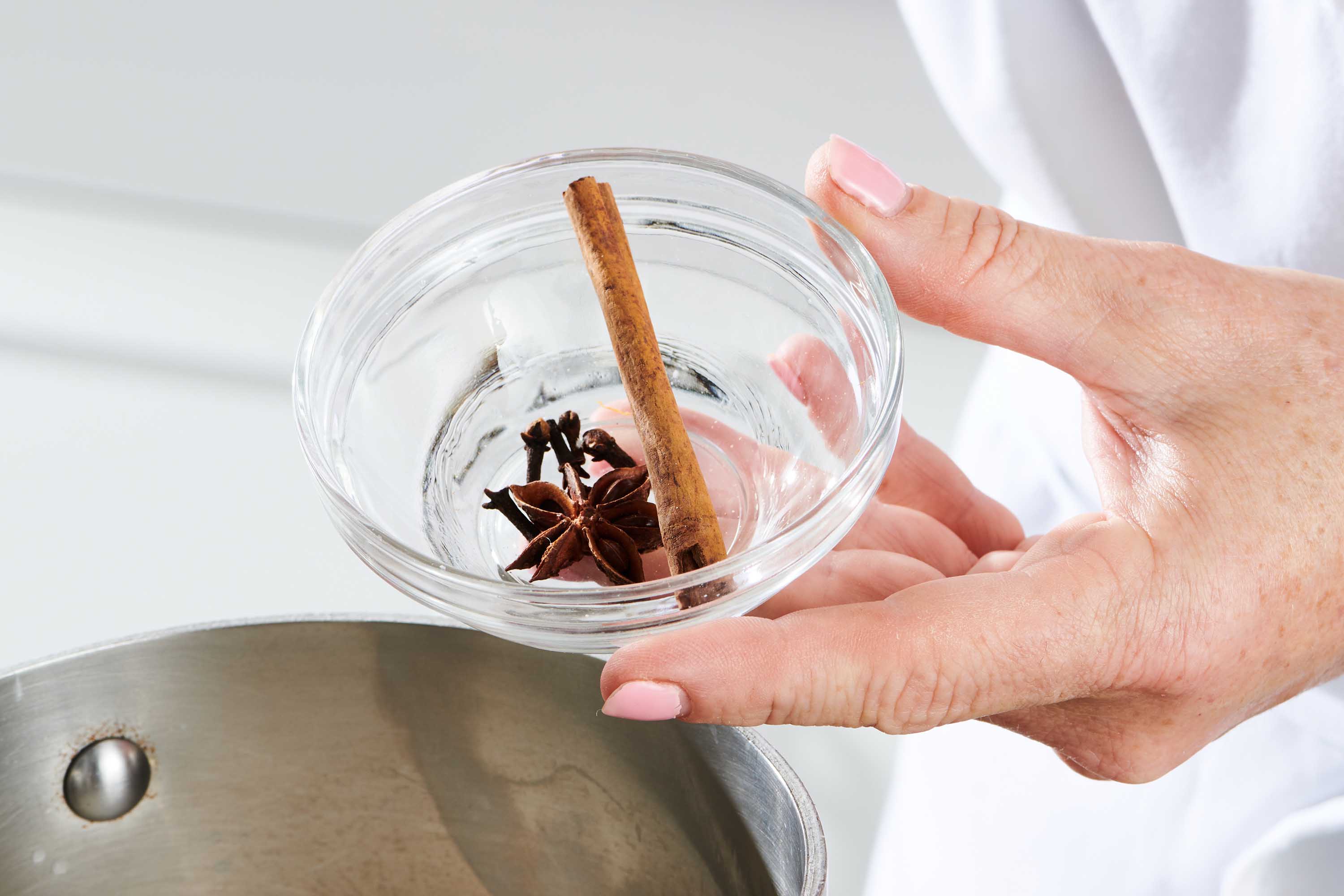 Woman holding a small glass bowl with a cinnamon stick, a star anise, and cloves.
