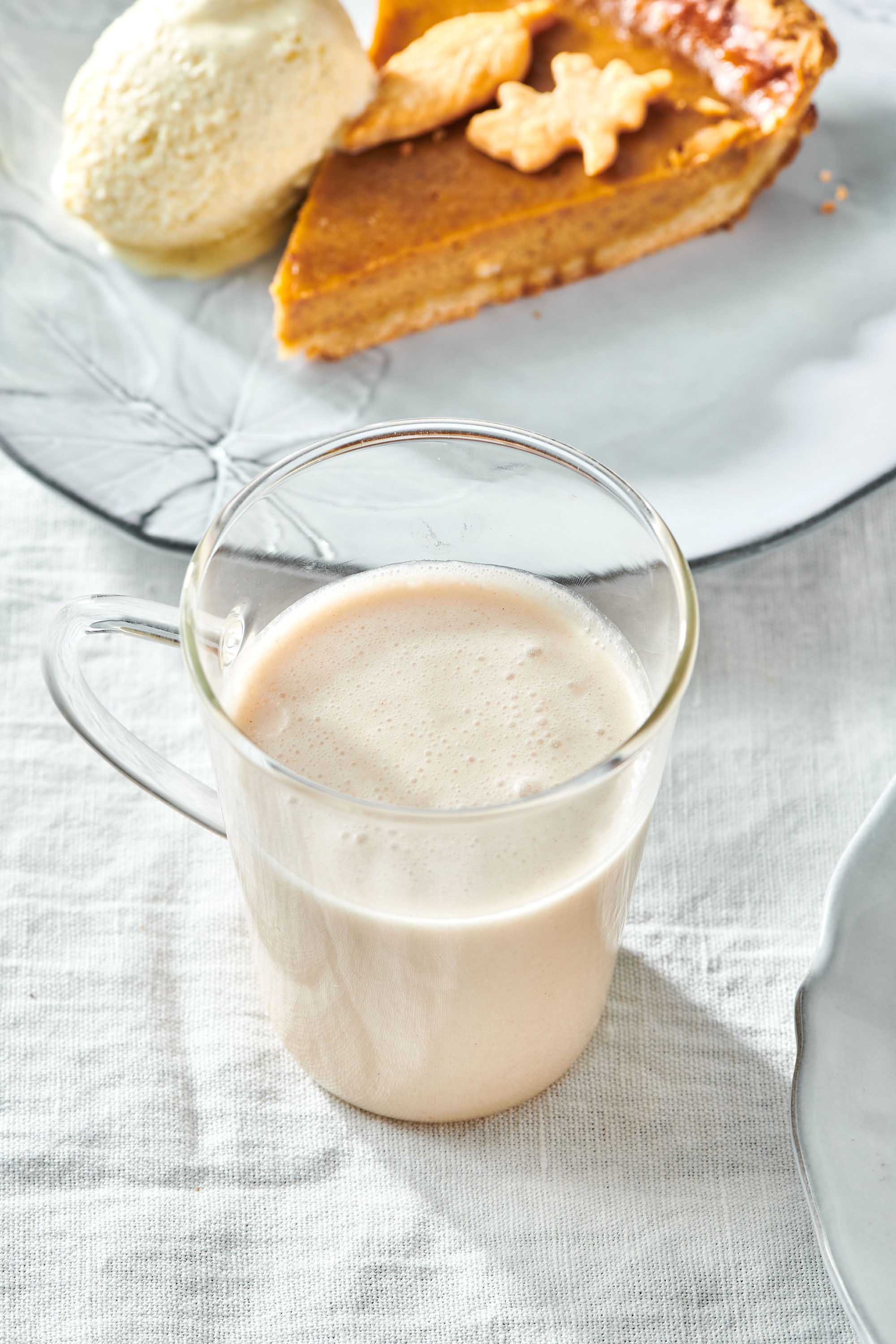 Glass mug of Coquito on a table with a slice of pie.