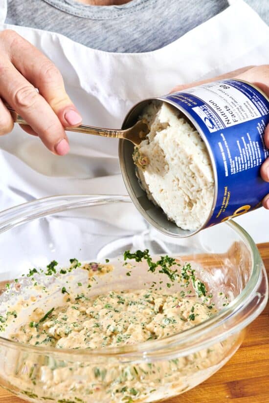 Woman using a spoon to get crabmeat from a can.