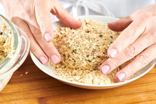 Woman dredging a crab cake in crushed saltines.