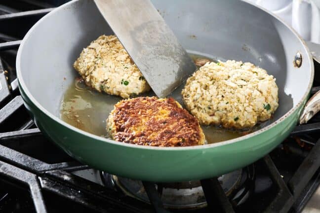 Spatula flipping crab cakes in a pan.