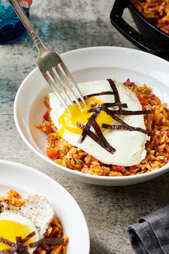Fork stabbing an egg on a bed of Kimchi Fried Rice.