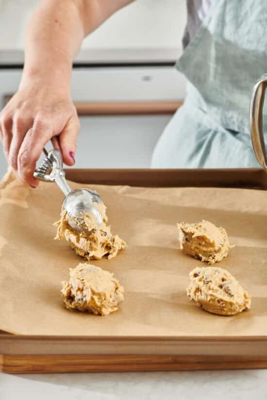 Woman scooping balls of cookie dough onto parchment paper.