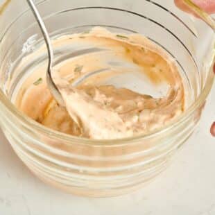 Spoon stirring a small glass bowl of Remoulade Sauce.