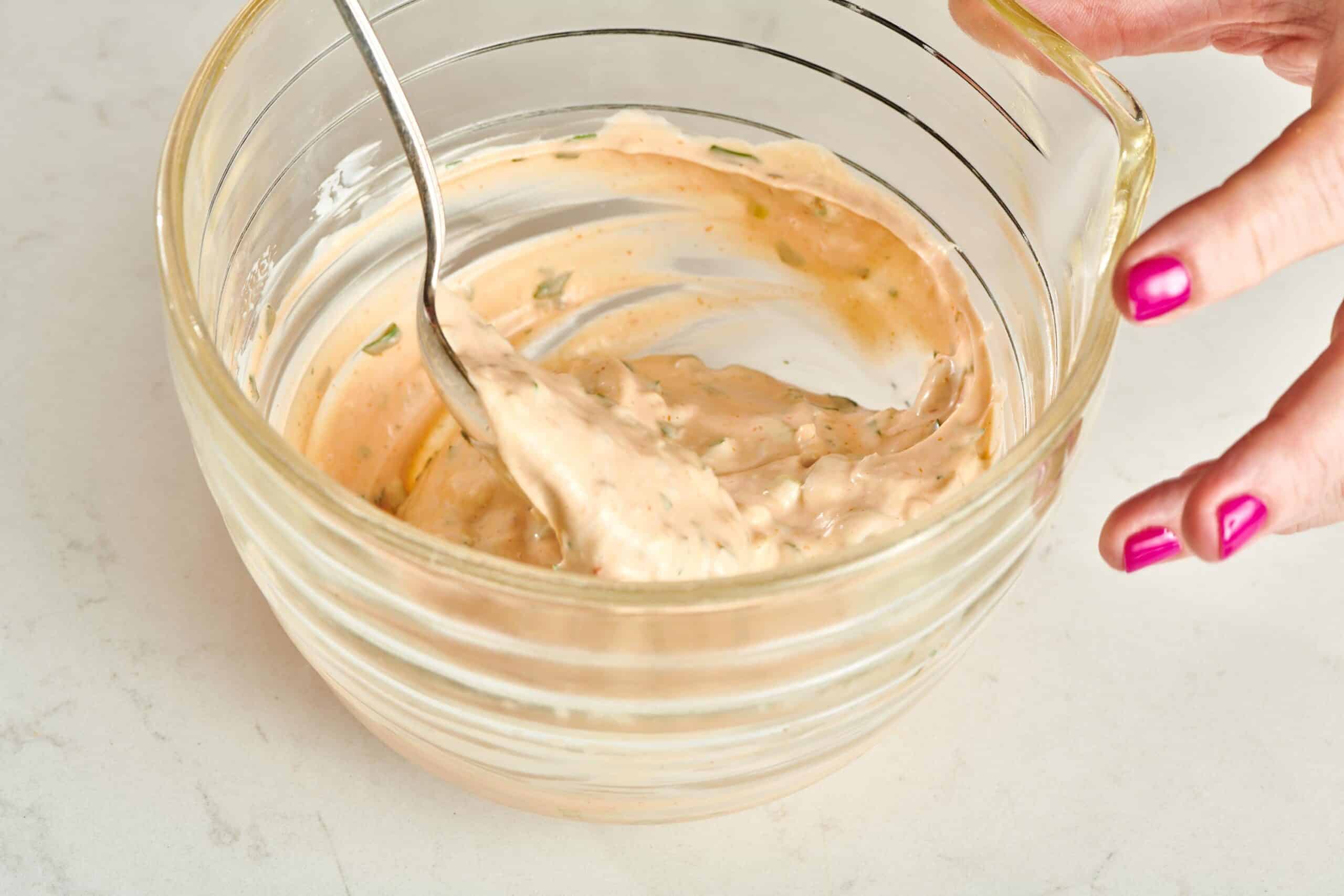 Woman stirring Remoulade Sauce in a glass bowl.