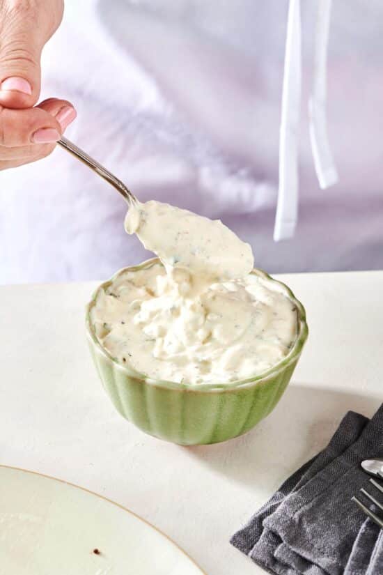 Spoon scooping Tartar Sauce from a small bowl.