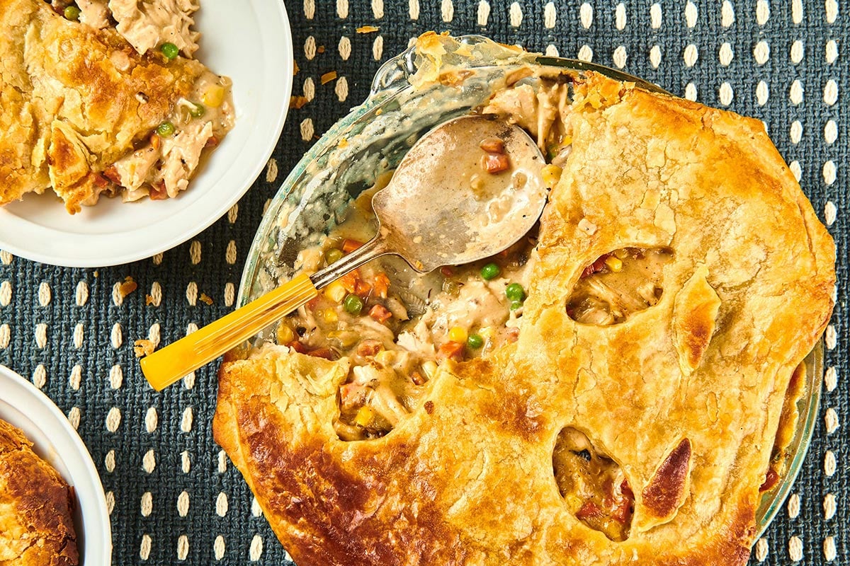 Spoon with turkey pot pie on table with plates.